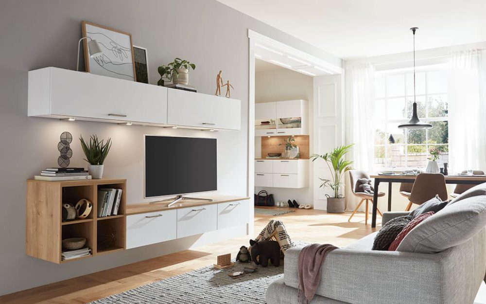 SIKO Bílý obývákový nábytek s chomovými úchytkami v kombinaci s dřevodekorem a otevřenými skříňkami a policemi k použití i v chodbě.