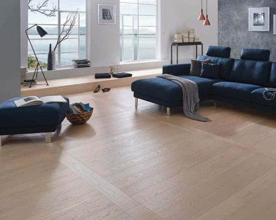 SIKO Moderná obývačka s netradičnou pokládkou drevenej podlahy. Tmavomodrá pohovka a originálne steny ladia s drevenou podlahou.