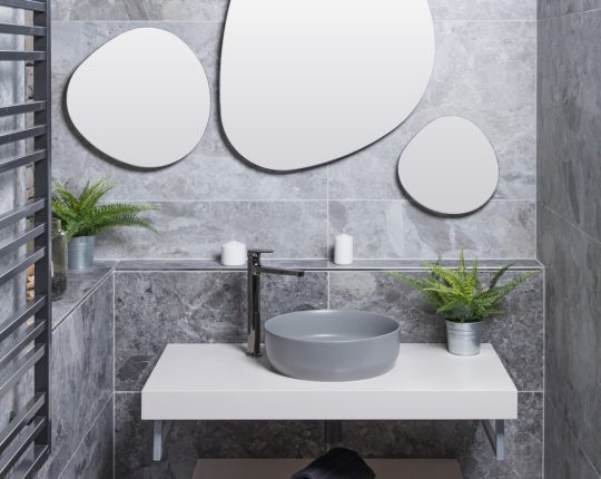 SIKO Asymetrické zrcadlo v malé koupelně, kamenné obklady, šedé umyvadlo na desku.