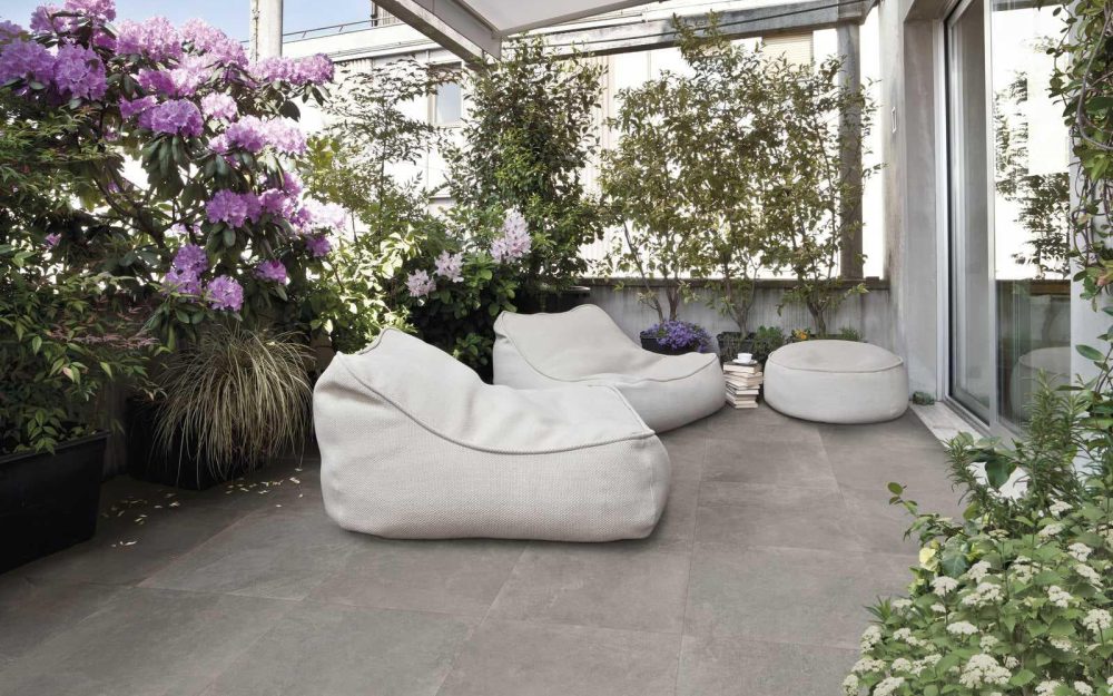 SIKO Dlažba v dizajne cement betón na terase so sedacími vankúšmi a s kvitnúcimi kvetmi pre dokonalý relax.