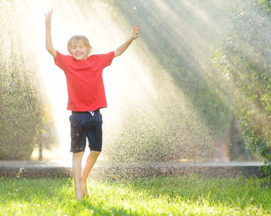 SIKO Chlapec radující se z osvěžení zahradní sprchou na zahradě během teplého letního dne