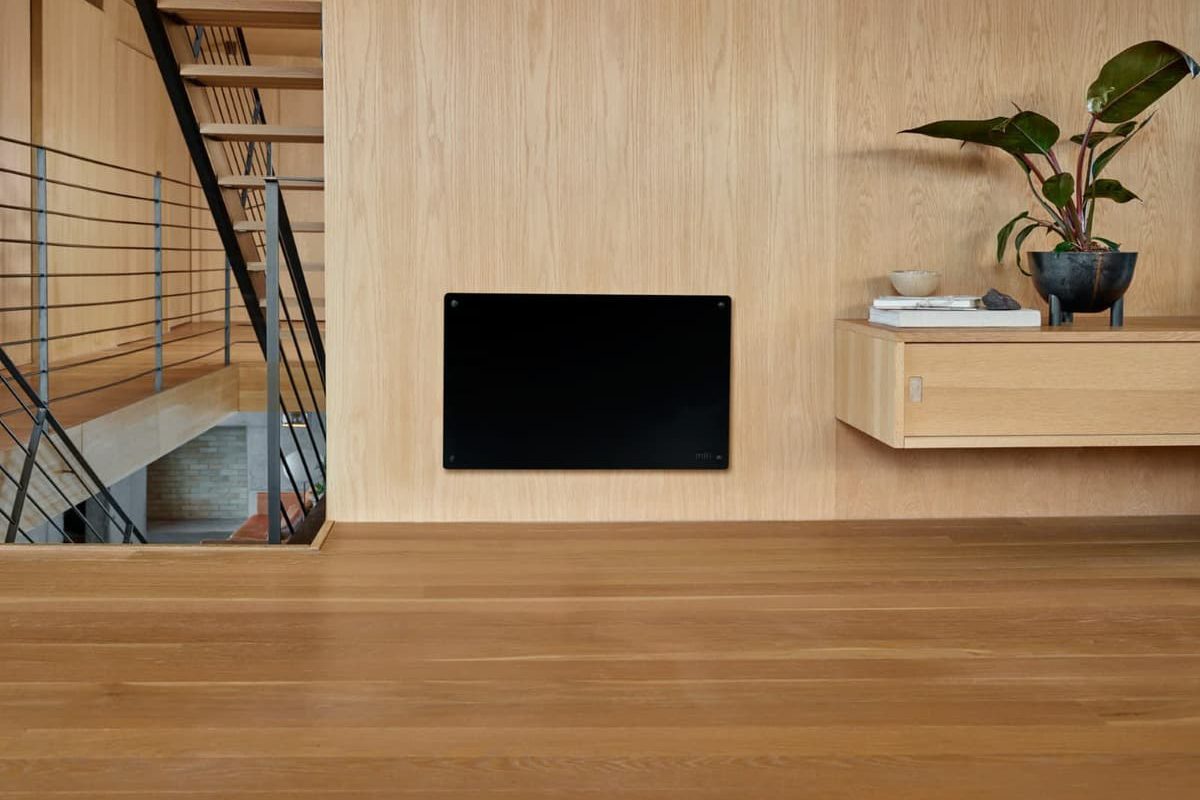 SIKO Čierny vykurovací panel v drevenom interiéri. Stena obložená svetlým drevom, drevená podlaha.