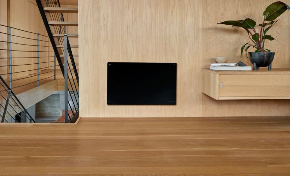 SIKO_Černý topný panel v dřevěném interiéru. Stěna obložená světlým dřevem, dřevěná podlaha.
