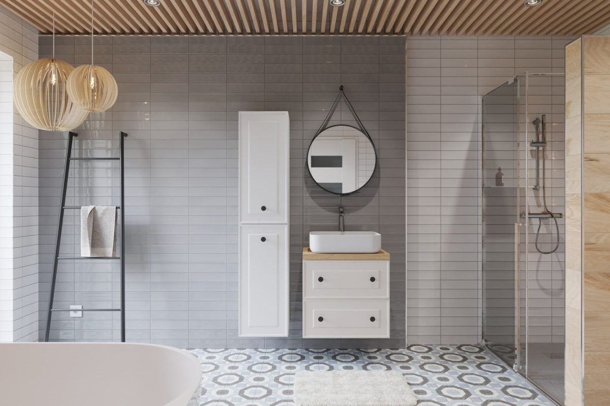 SIKO_Hygge atmosféra ve velké koupelně, světlé obklady, dlažba v designu patchworku, dřevěné obklady, kulaté zrcadlo, bílý nábytek.