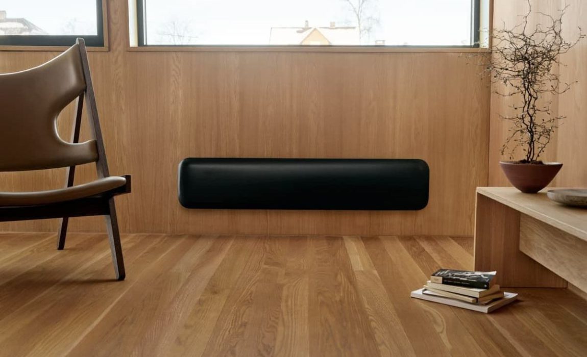 SIKO_Topný sálavý obdélníkový infrapanel v černé barvě. Interiér obložený dřevem, dřevvěná podlaha, moderní kožené křeslo.