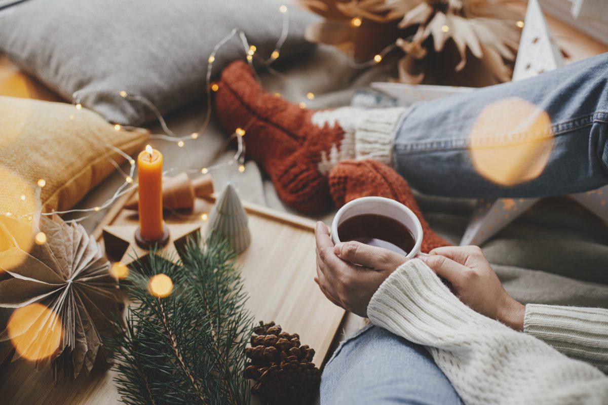 SIKO_Hygge atmosféra, množstvo doplnkov vo vianočnom štýle, zapálené sviečky, svetielka, teplé ponožky a šálka horúceho čaju.